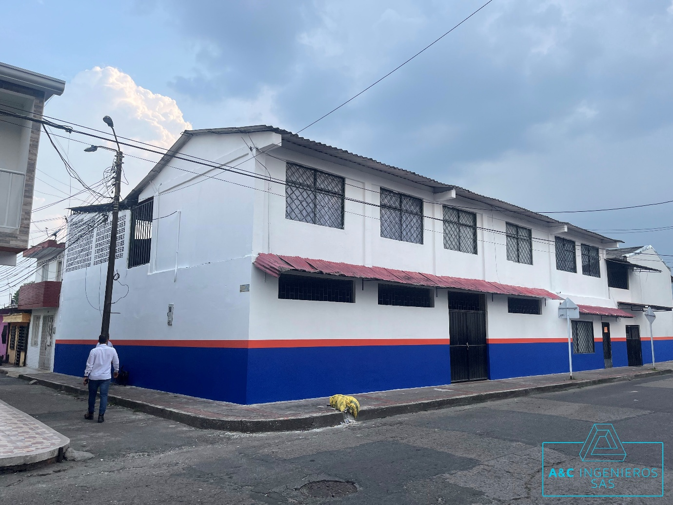 Edificio blanco y azul con detalles rojos en una esquina de la calle, una persona pasa caminando.
