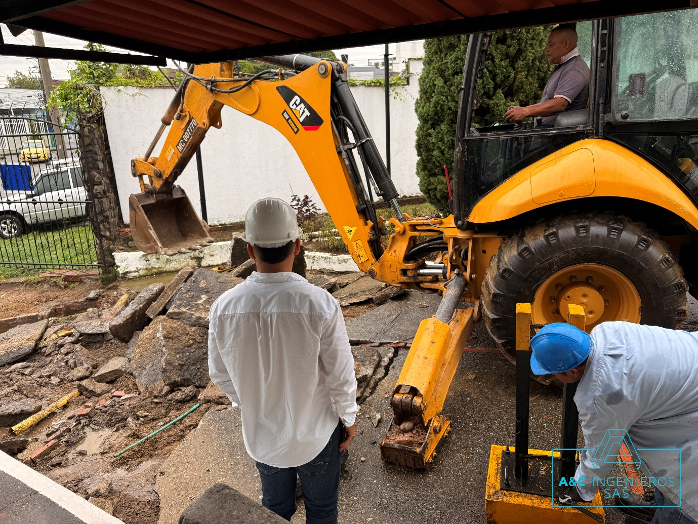 Hombres trabajando con una retroexcavadora en un sitio de construcción; uno opera la maquinaria, otro evalúa los daños.