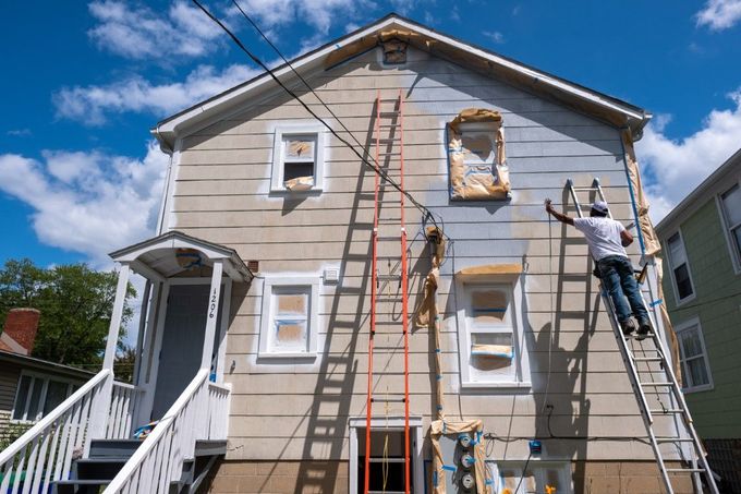 A man is painting the side of a house with a ladder.