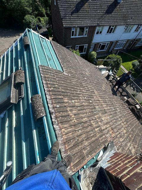 View from above of a roof being repaired.  A worker is seen on the right side.
