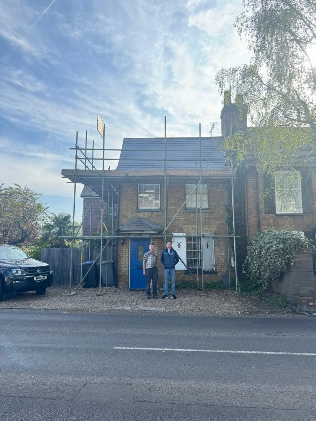 Two men stand in front of a house under construction, with scaffolding.