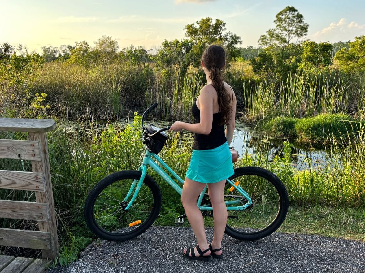 Woman with a teal bike stands by a marsh, looking at the view.