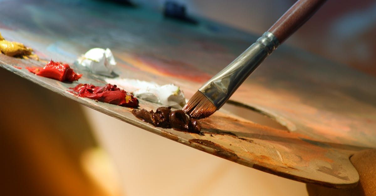 Close-up of an artist's palette with dabs of paint and a brush mixing brown.