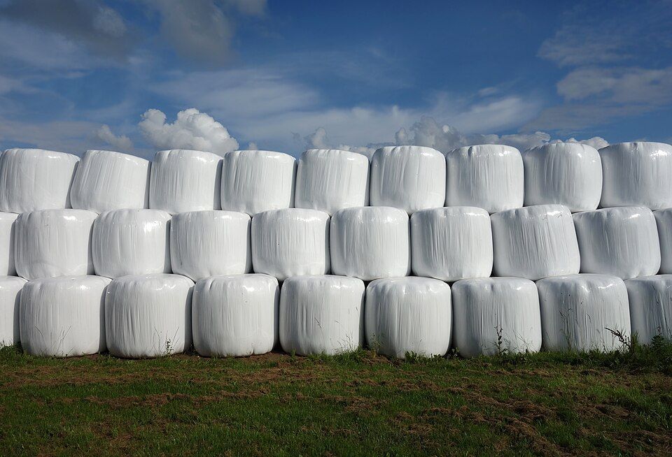 A stack of hay bales wrapped in plastic in a field.