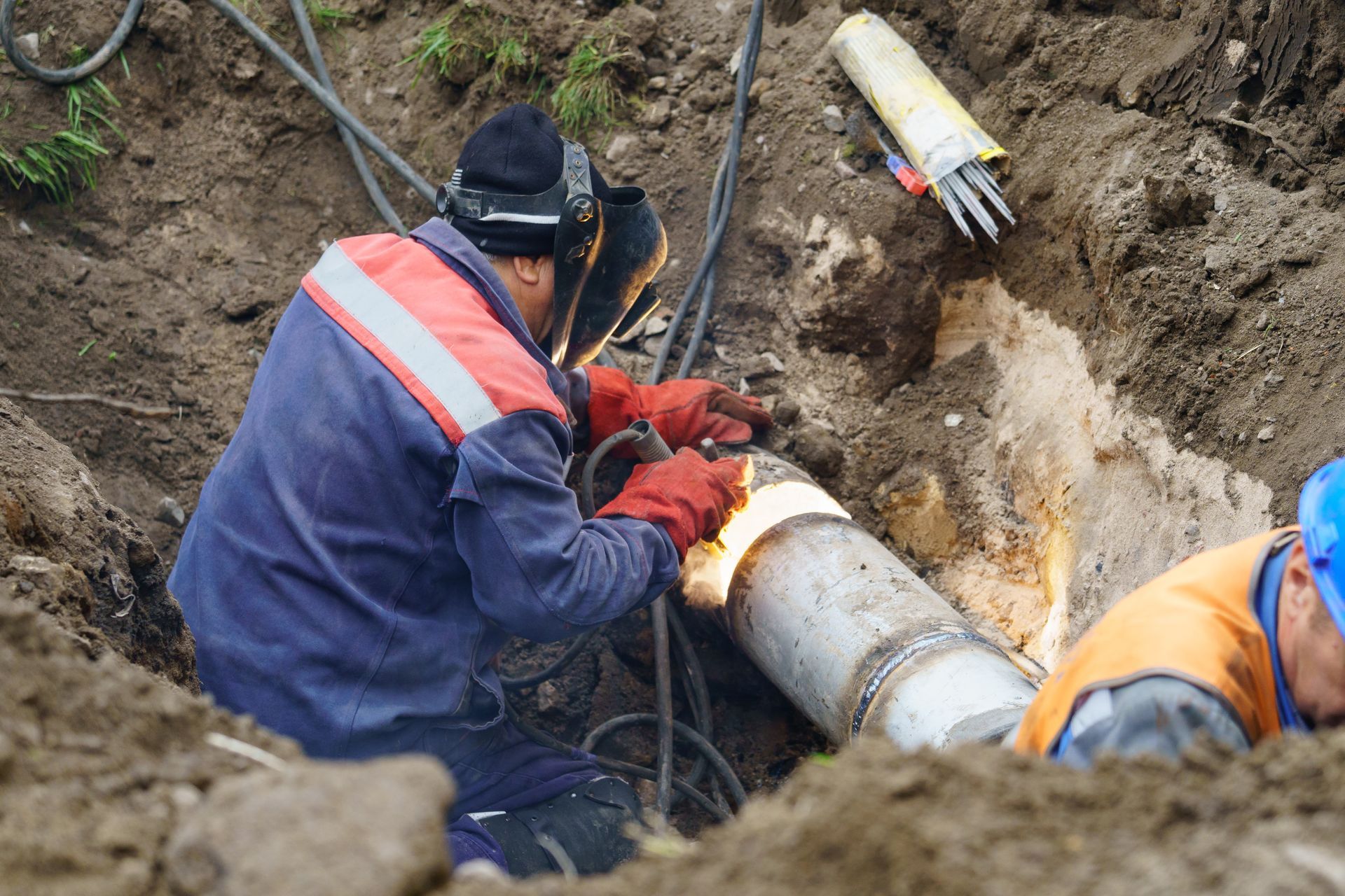 Utility worker welding to repair a broken water main, replacing damaged sections of the water pipe.