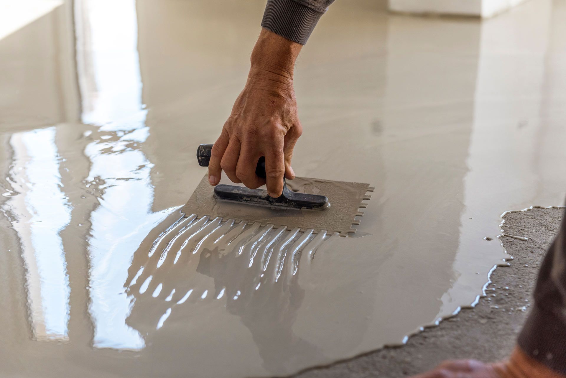 Person using a notched trowel to spread a thin-set mortar on a floor.