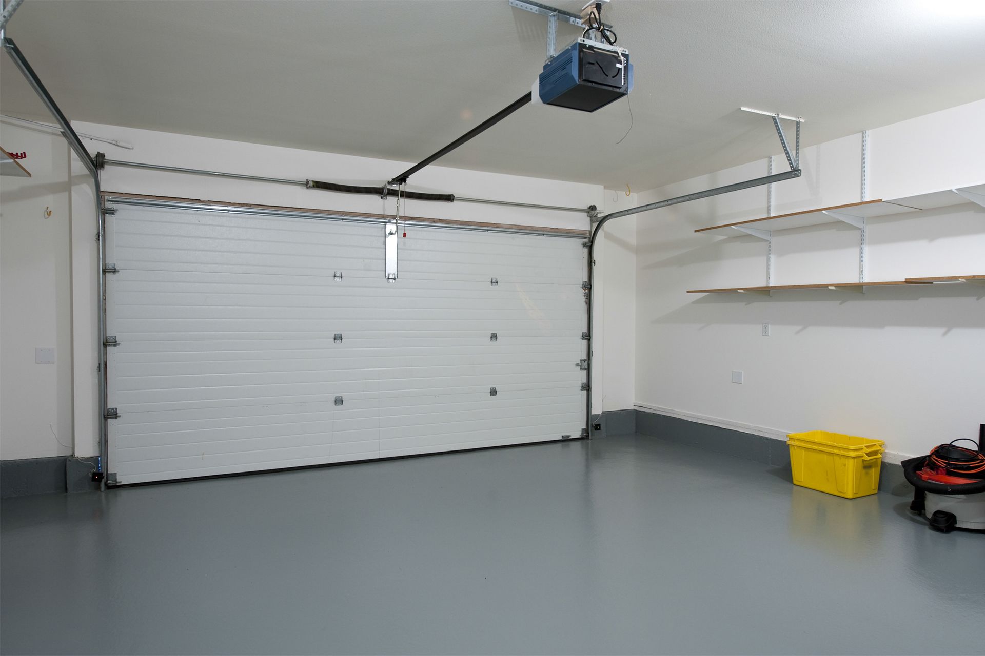 Empty garage with white door, gray floor, and yellow container.