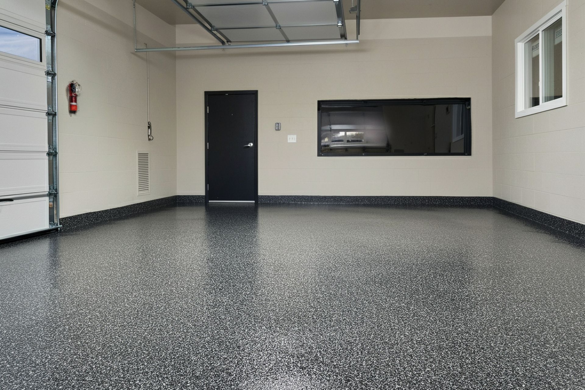 A clean garage with a speckled floor, black door, and window.