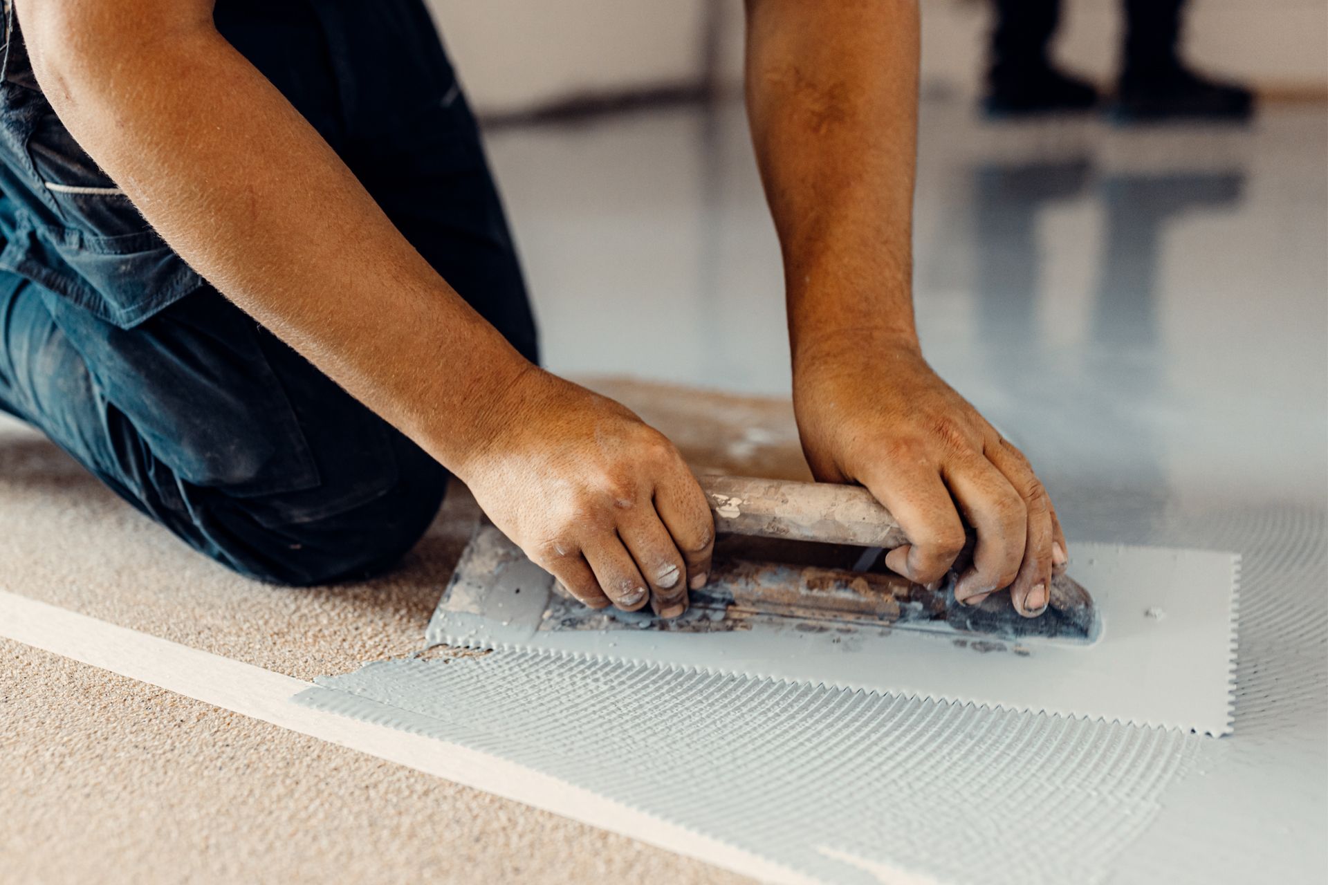 Person kneeling, smoothing epoxy flooring with a trowel; indoors.
