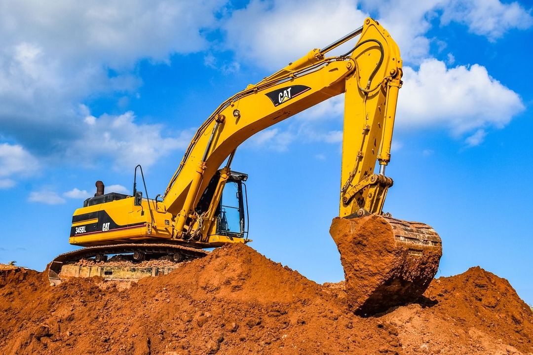 a yellow cat excavator is digging a pile of dirt