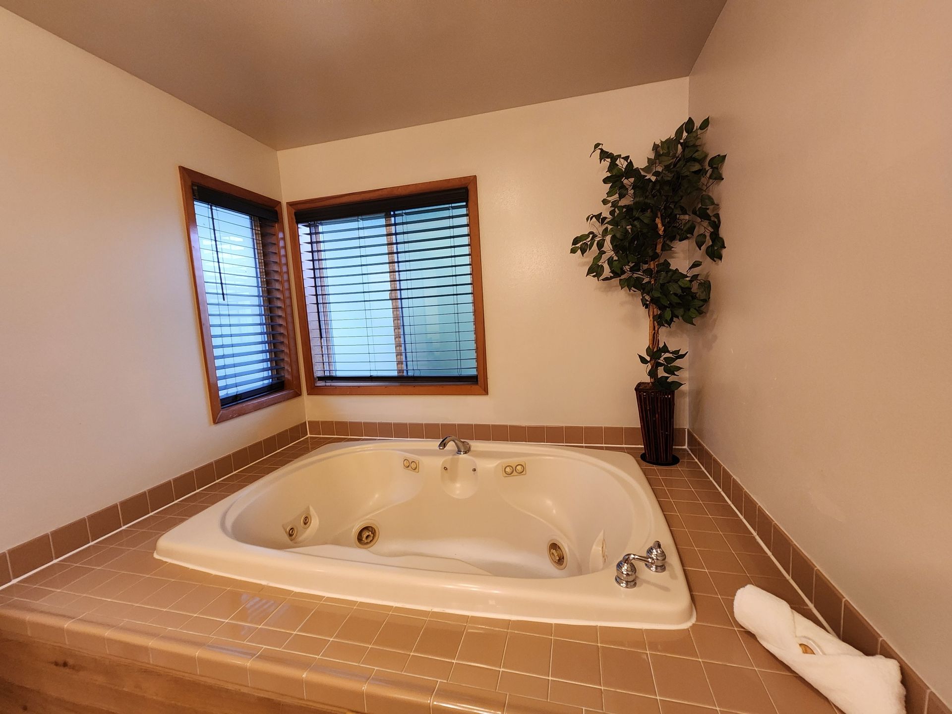 A jacuzzi tub in a room with a window, tile floor, and a potted plant. A towel sits on the edge.