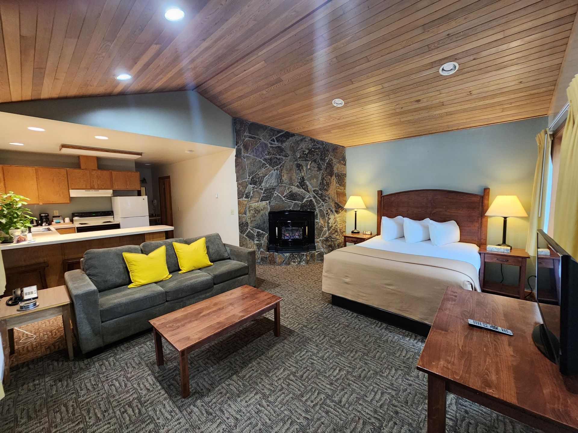 Cozy hotel suite with a fireplace, king bed, sofa, kitchenette, and wooden accents.