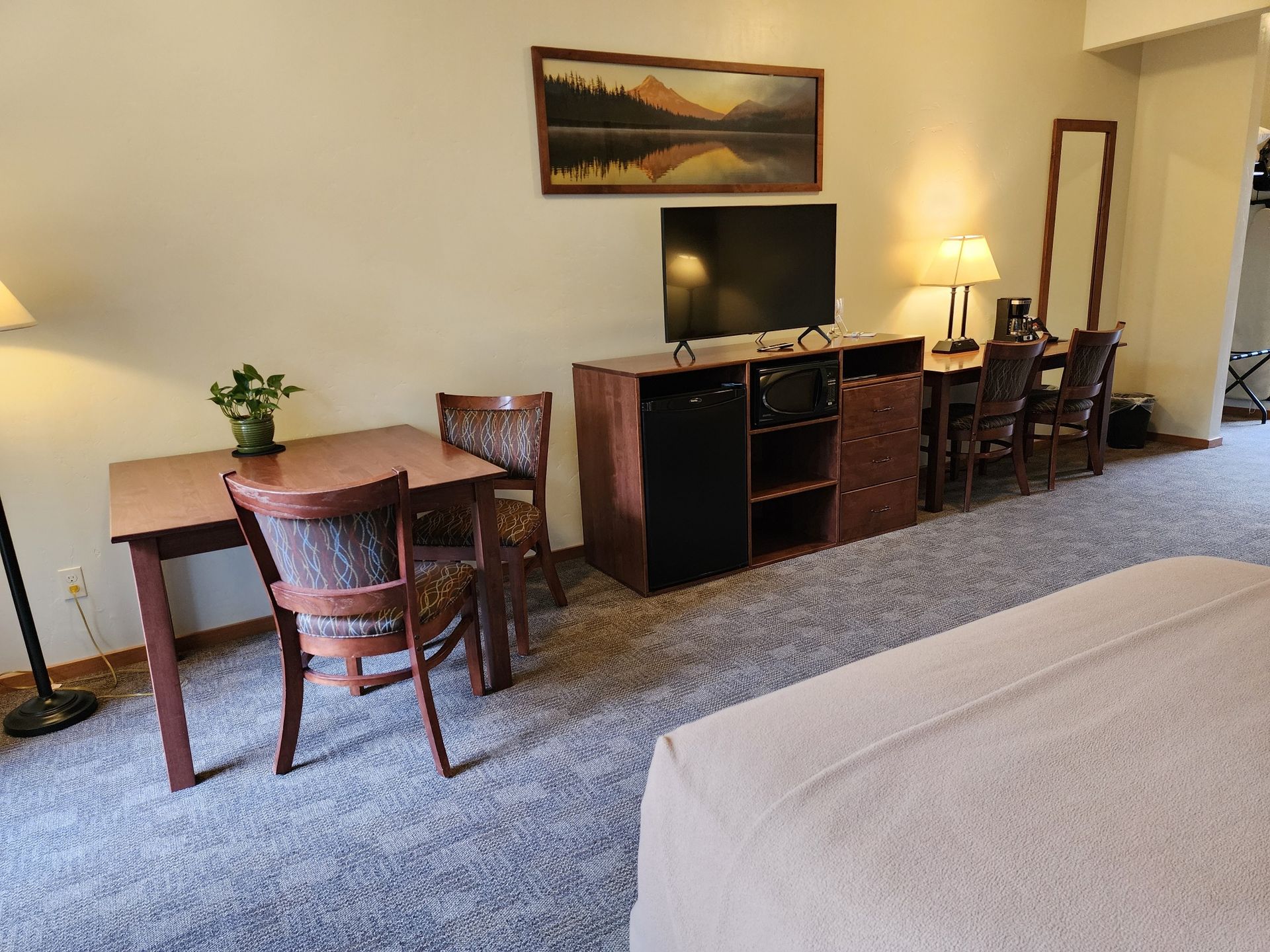 A hotel room with a bed, TV, dining table and chairs, and a mirror.