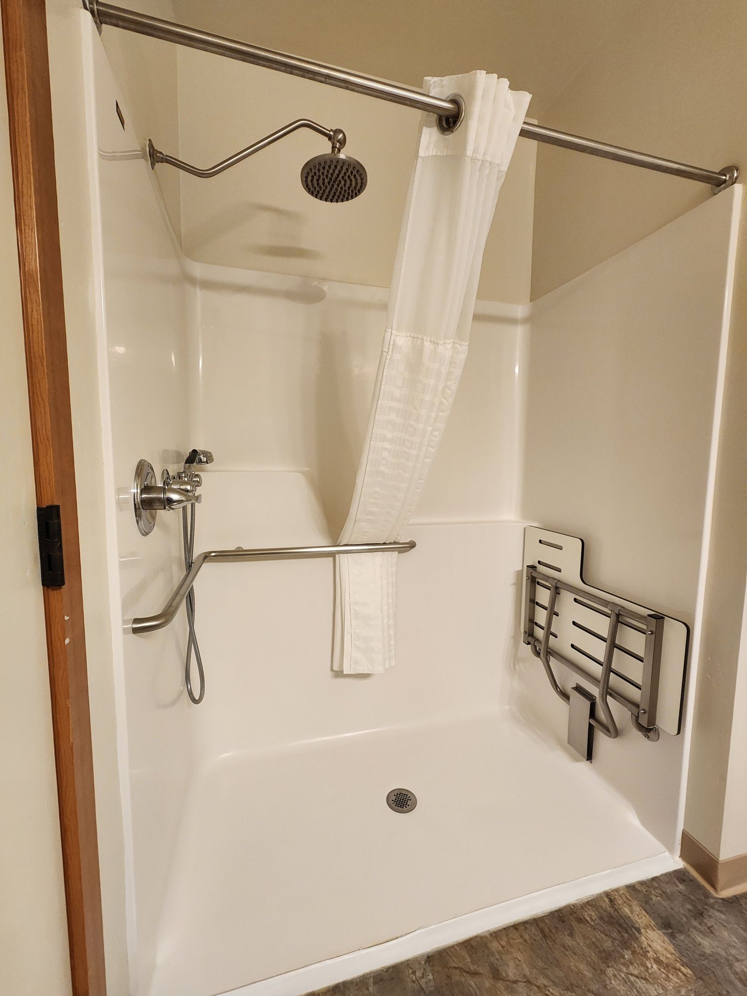 White accessible shower stall with safety bars, a fold-down seat, and a shower curtain.