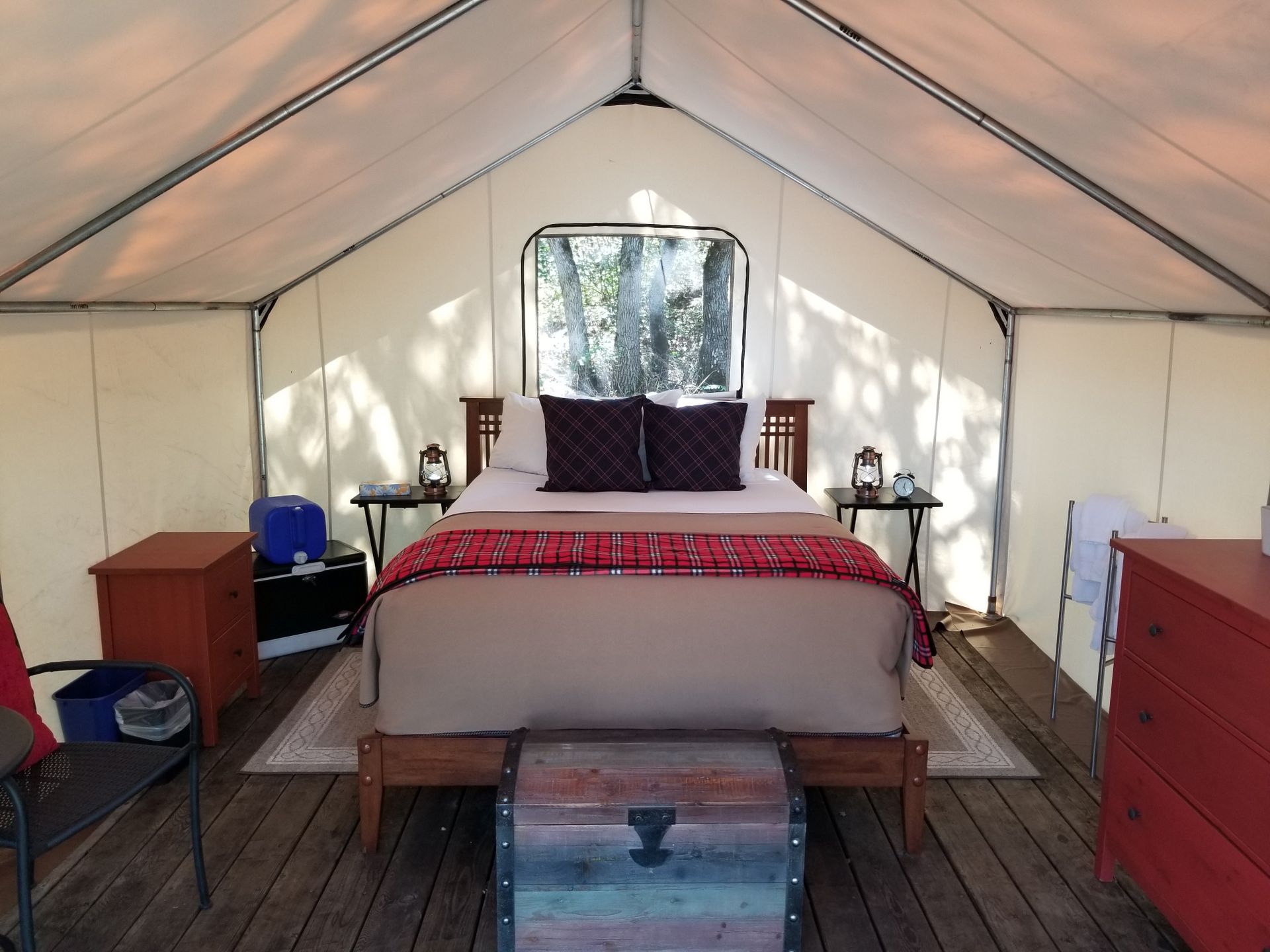 Inside of a glamping tent with bed, nightstands, and trunk. Red and brown hues.