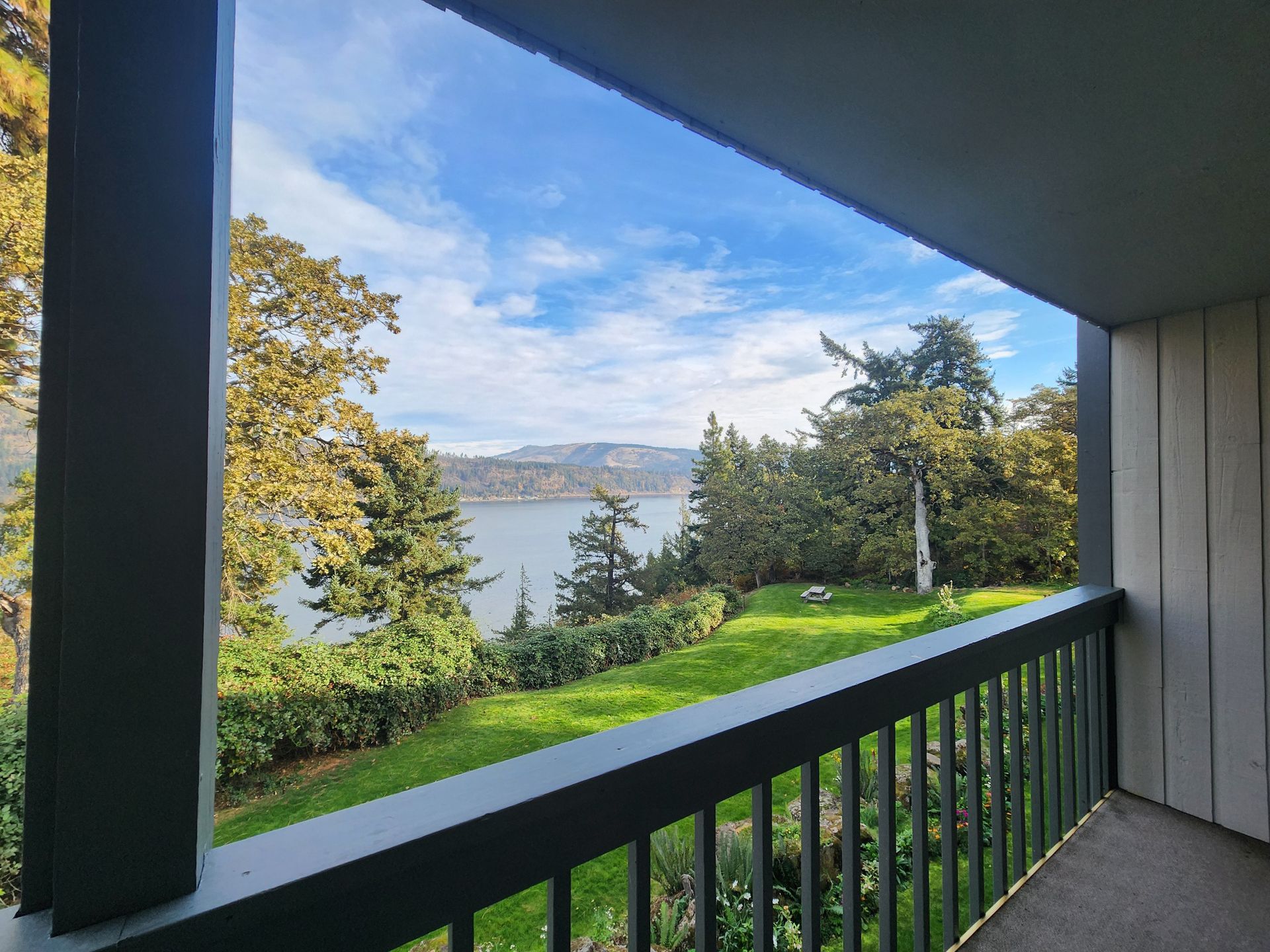 Balcony view overlooking a body of water, trees, and blue sky with clouds.