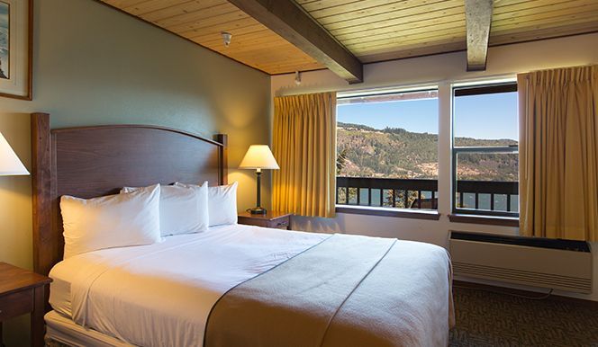 Bedroom with a bed, lamp, and window overlooking a mountainous landscape.