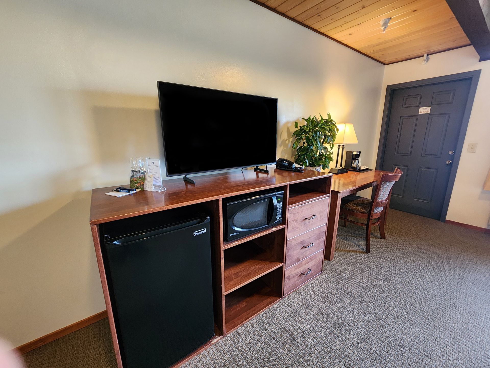 Hotel room with a TV, microwave, mini-fridge, desk, and door.