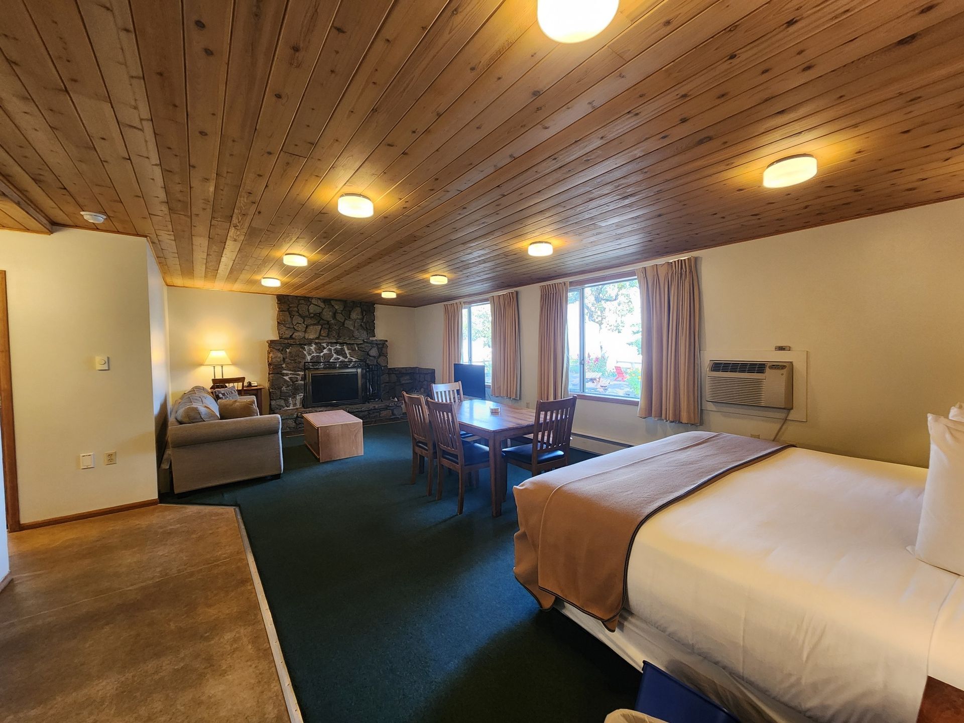 Spacious hotel room with a bed, dining area, fireplace, and wooden ceiling.