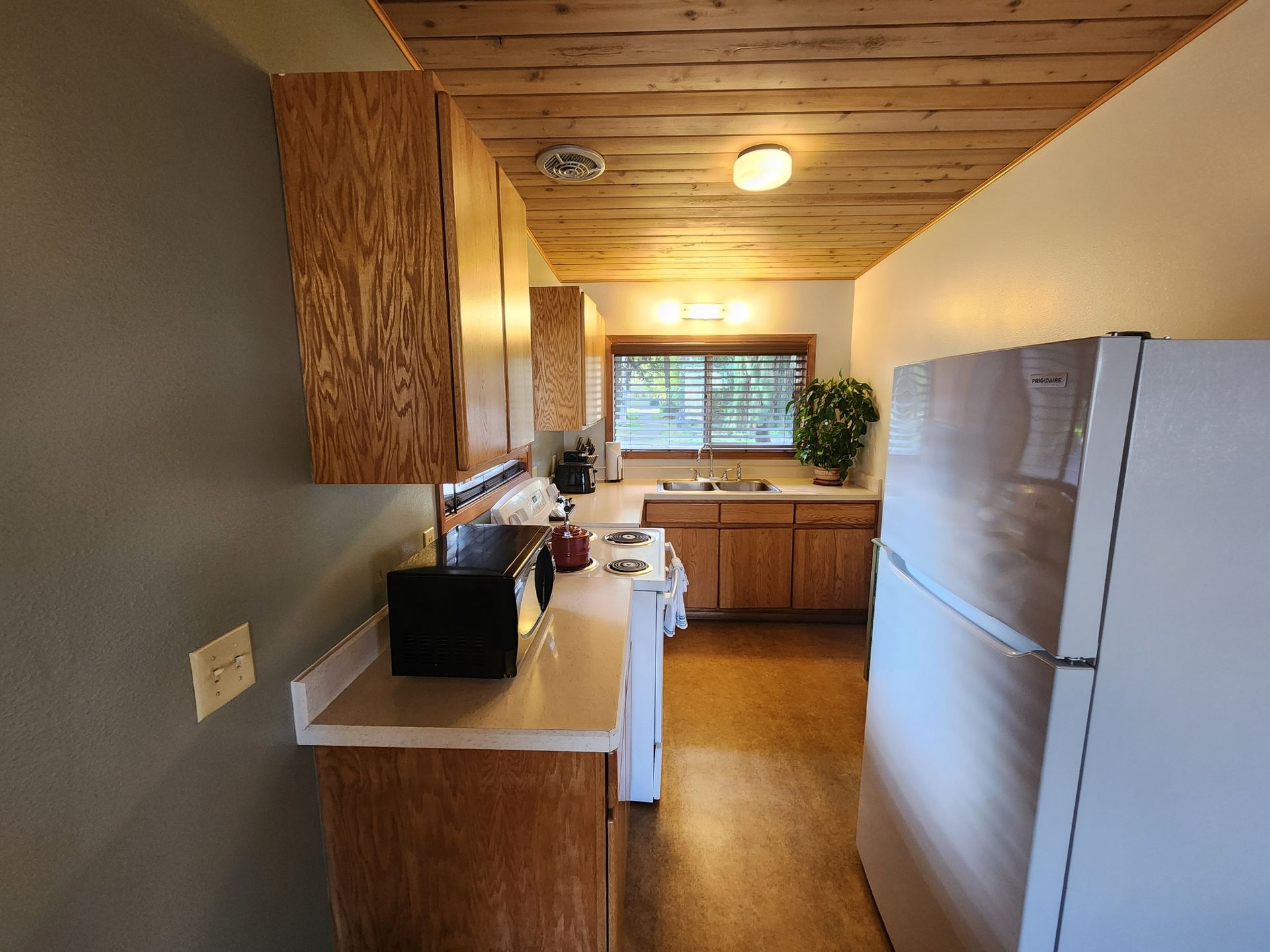 Kitchen with wood ceiling, cabinets, appliances, and a window.