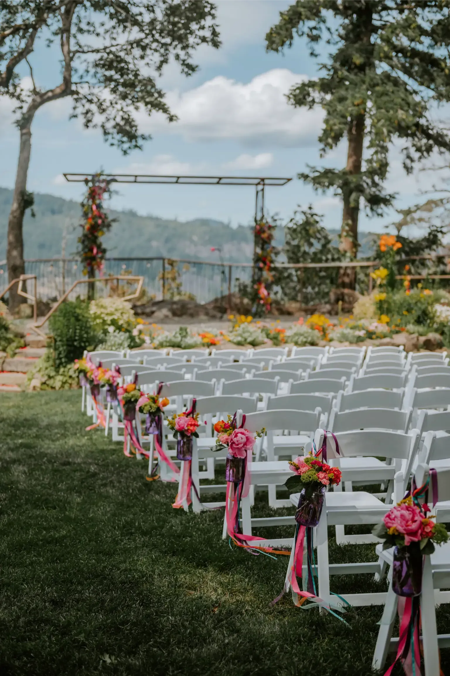 Wedding ceremony setup outdoors with white chairs, floral decorations, and a mountain view.