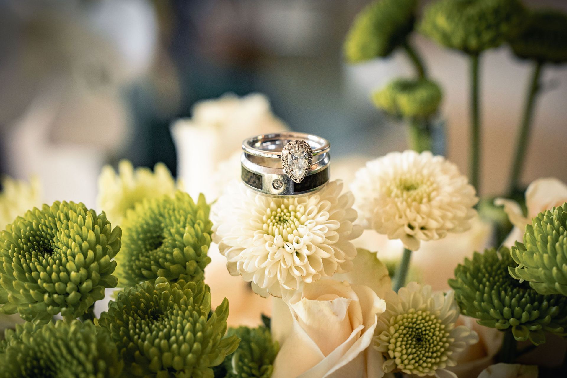 Wedding rings atop a bouquet of white and green flowers, soft focus background.