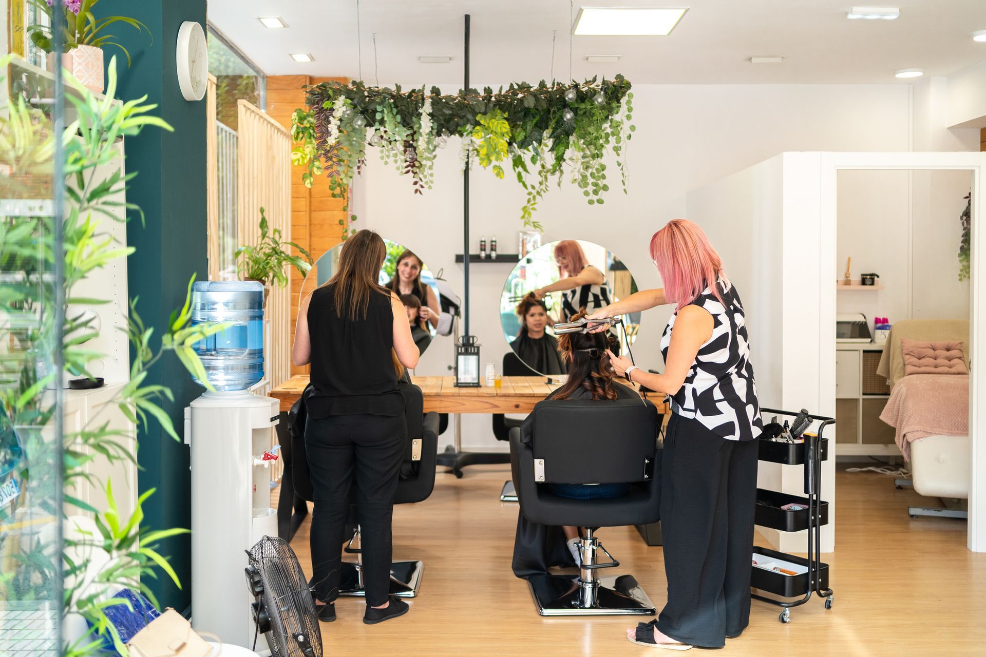 Hair salon interior: stylists working on clients, natural light, greenery, white walls, wooden surfaces.