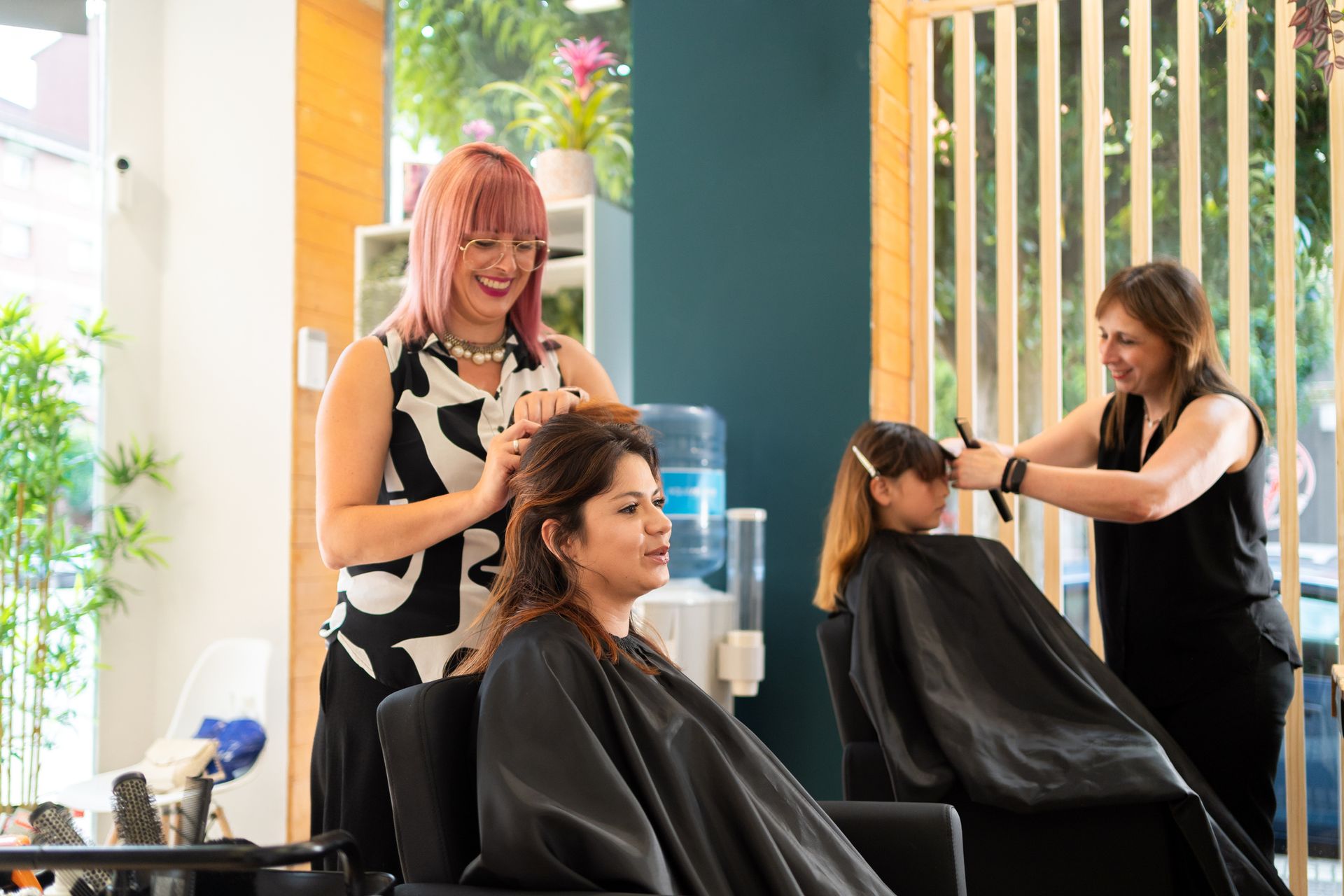 Three people in a hair salon: two stylists and two clients getting haircuts.