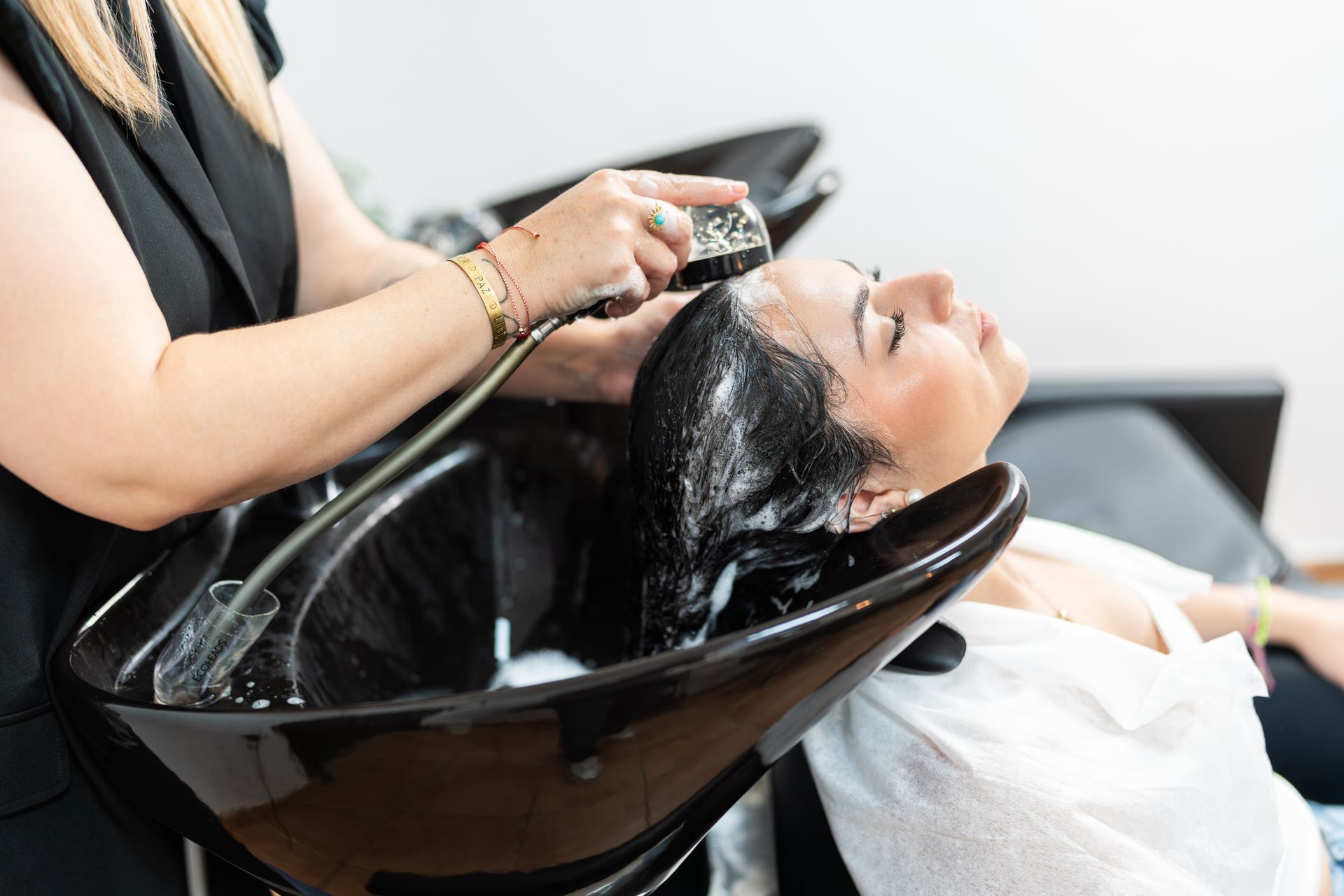 Hair stylist washing a woman's hair in a salon. Black sink, white shirt.
