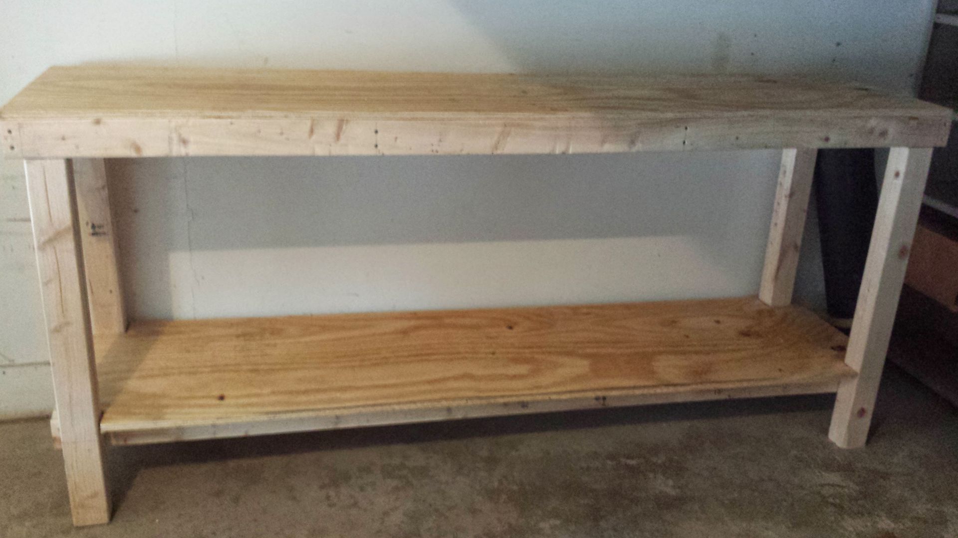 A wooden table with a shelf underneath it is sitting on the floor.