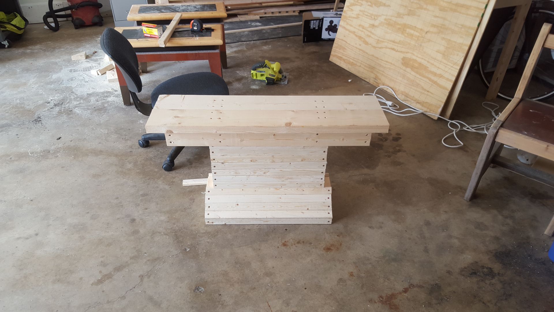 A wooden table is sitting in a garage next to a chair.