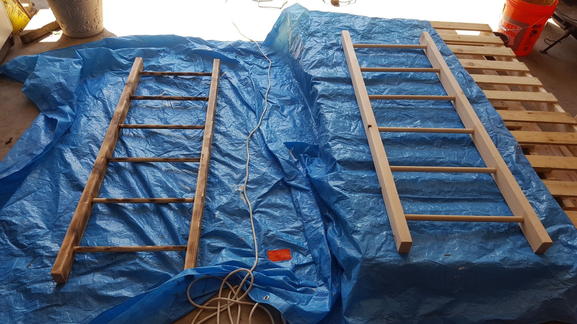 Two wooden ladders are sitting on top of a blue tarp.