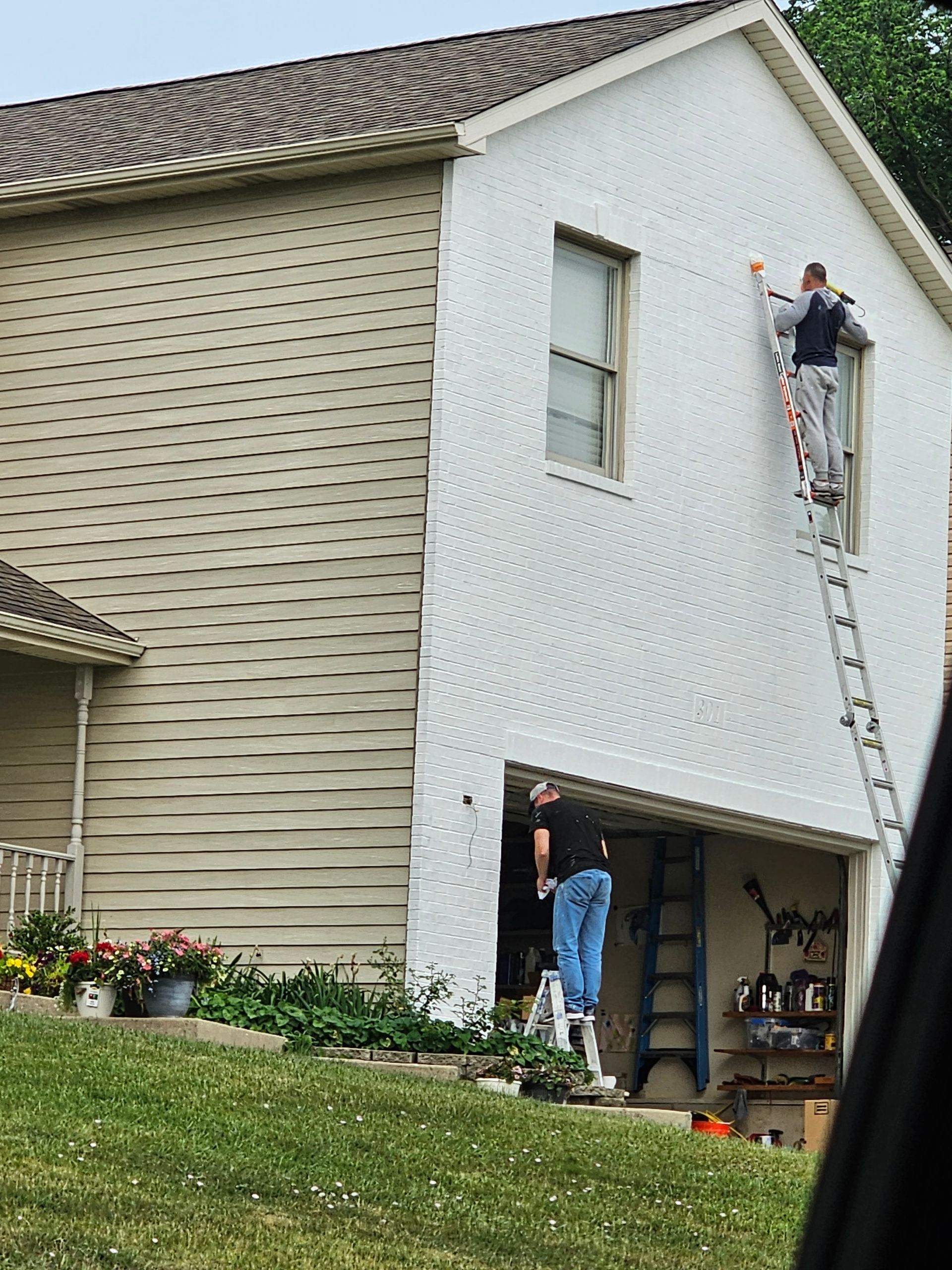 A man on a ladder is painting the side of a house