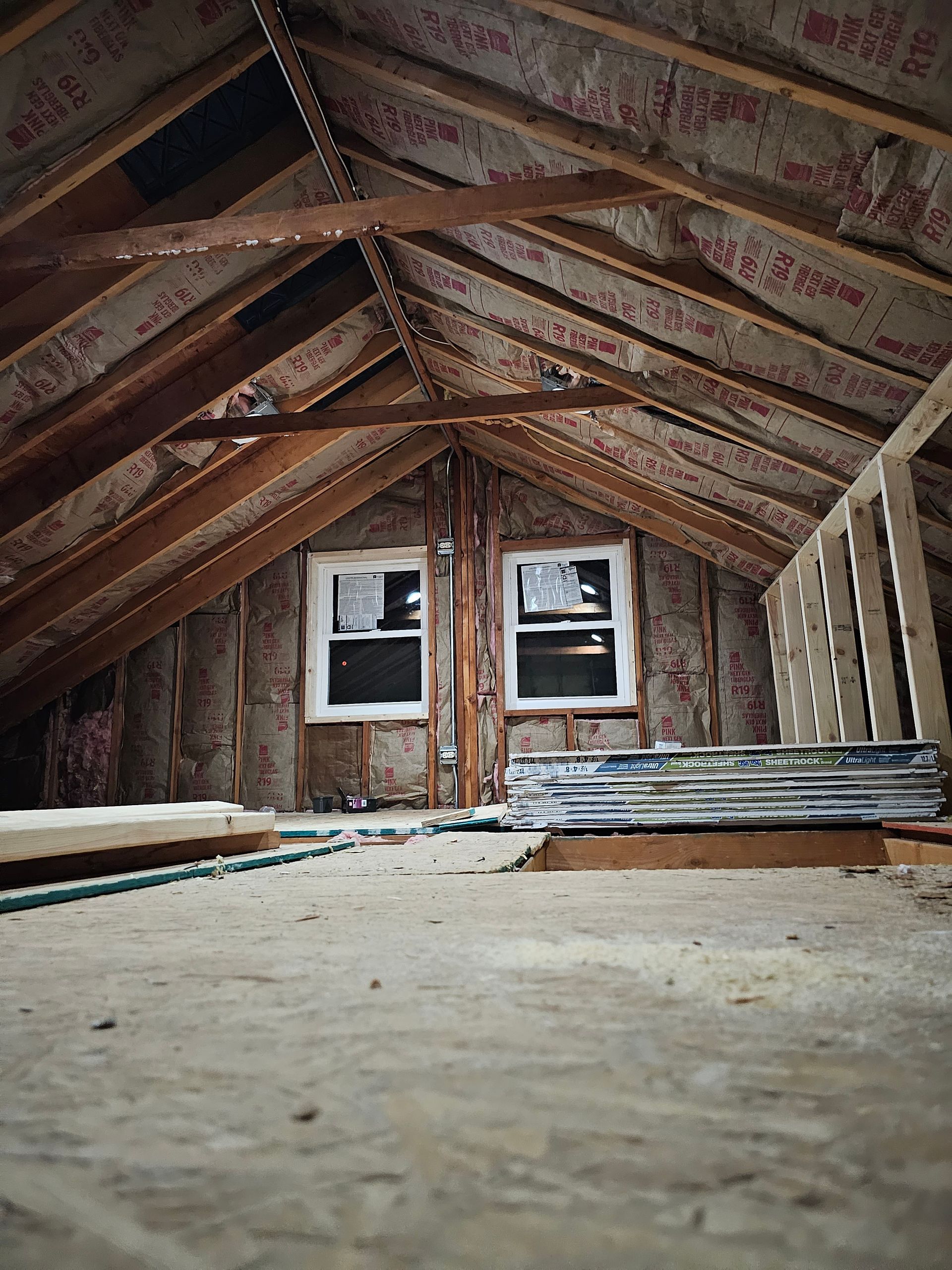 An attic under construction with insulation and two windows.