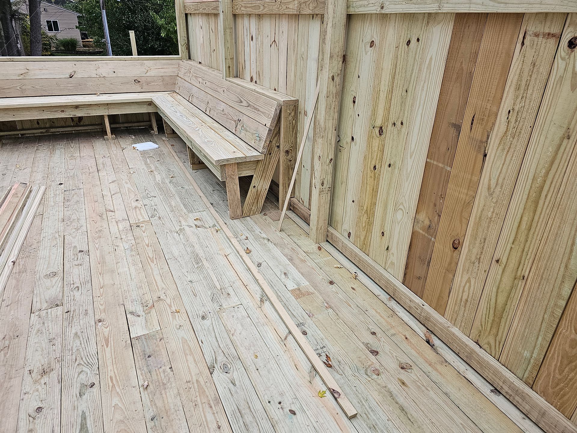 A wooden bench is sitting on a wooden deck next to a wooden fence.