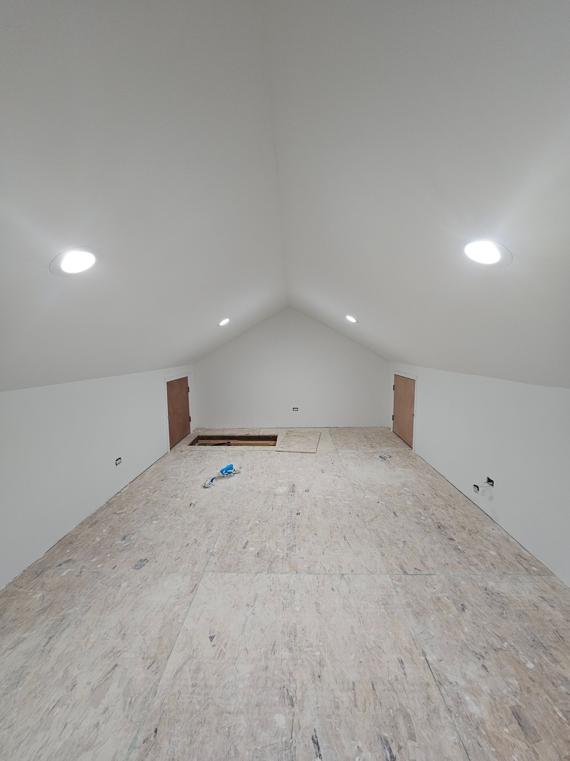 An empty attic with a vaulted ceiling and a wooden floor.