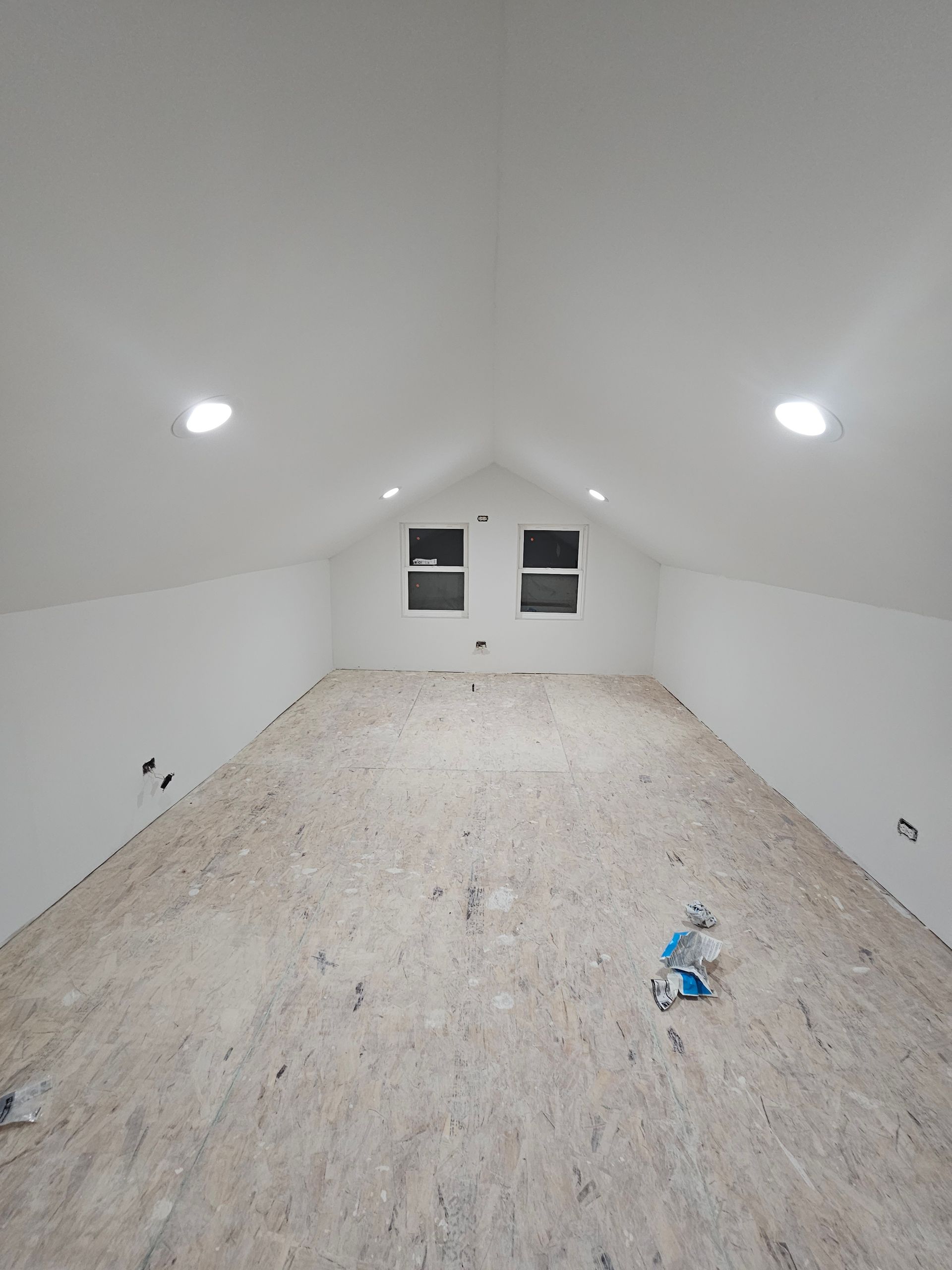 An empty attic with a wooden floor and white walls.