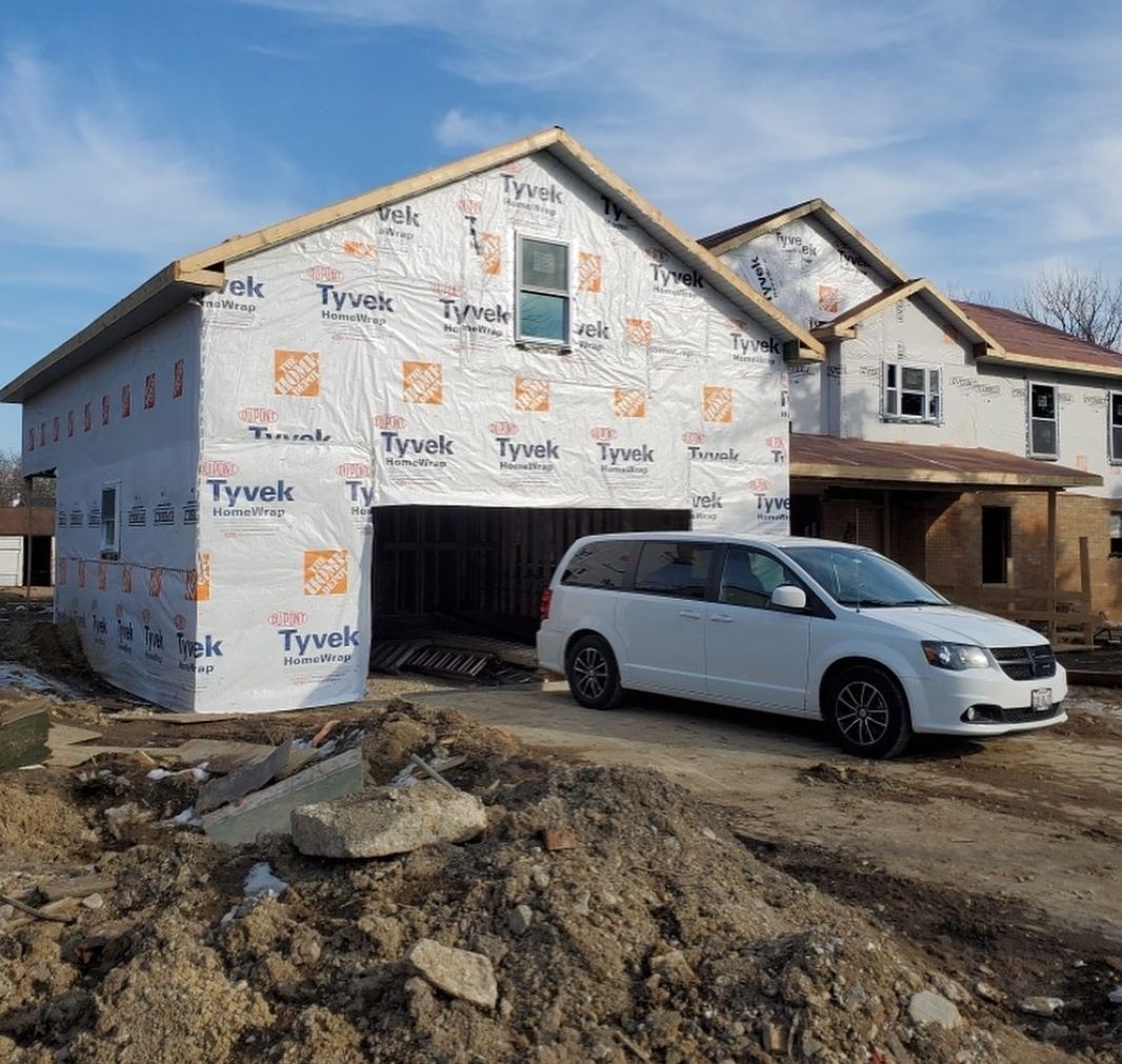 A white van is parked in front of a house under construction.
