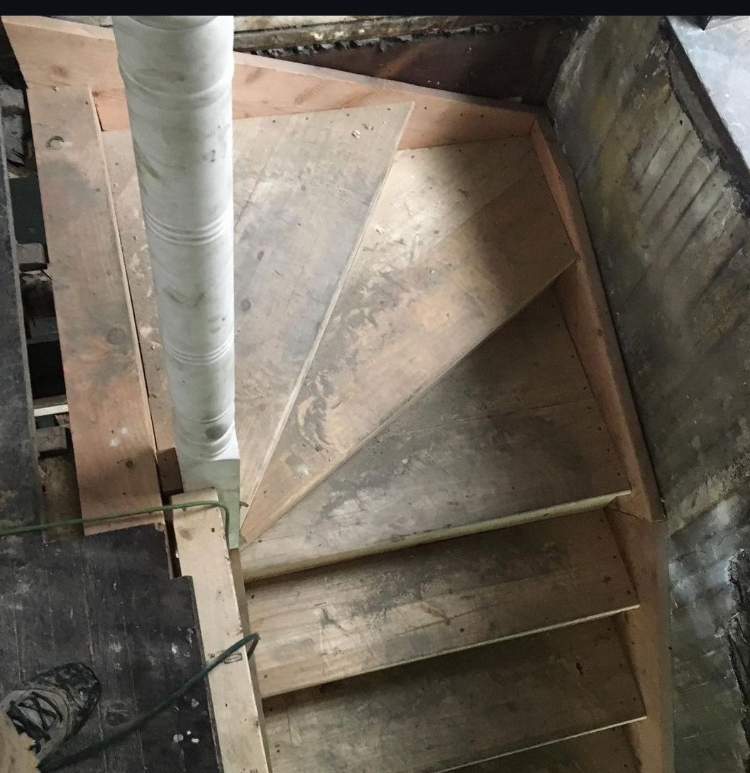 A wooden spiral staircase is being built in a basement.