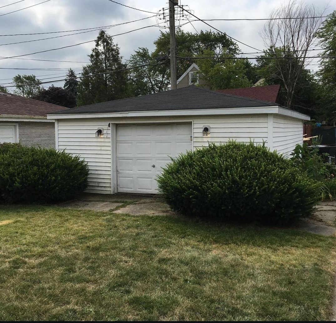 A white garage with a black roof sits in the middle of a lush green yard
