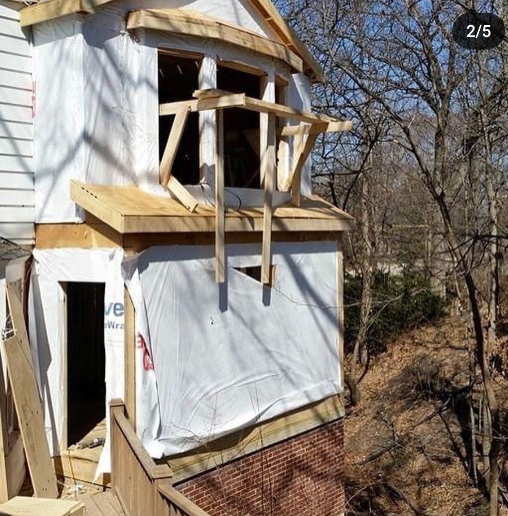 A house is being built on a hill with a fence and trees in the background.