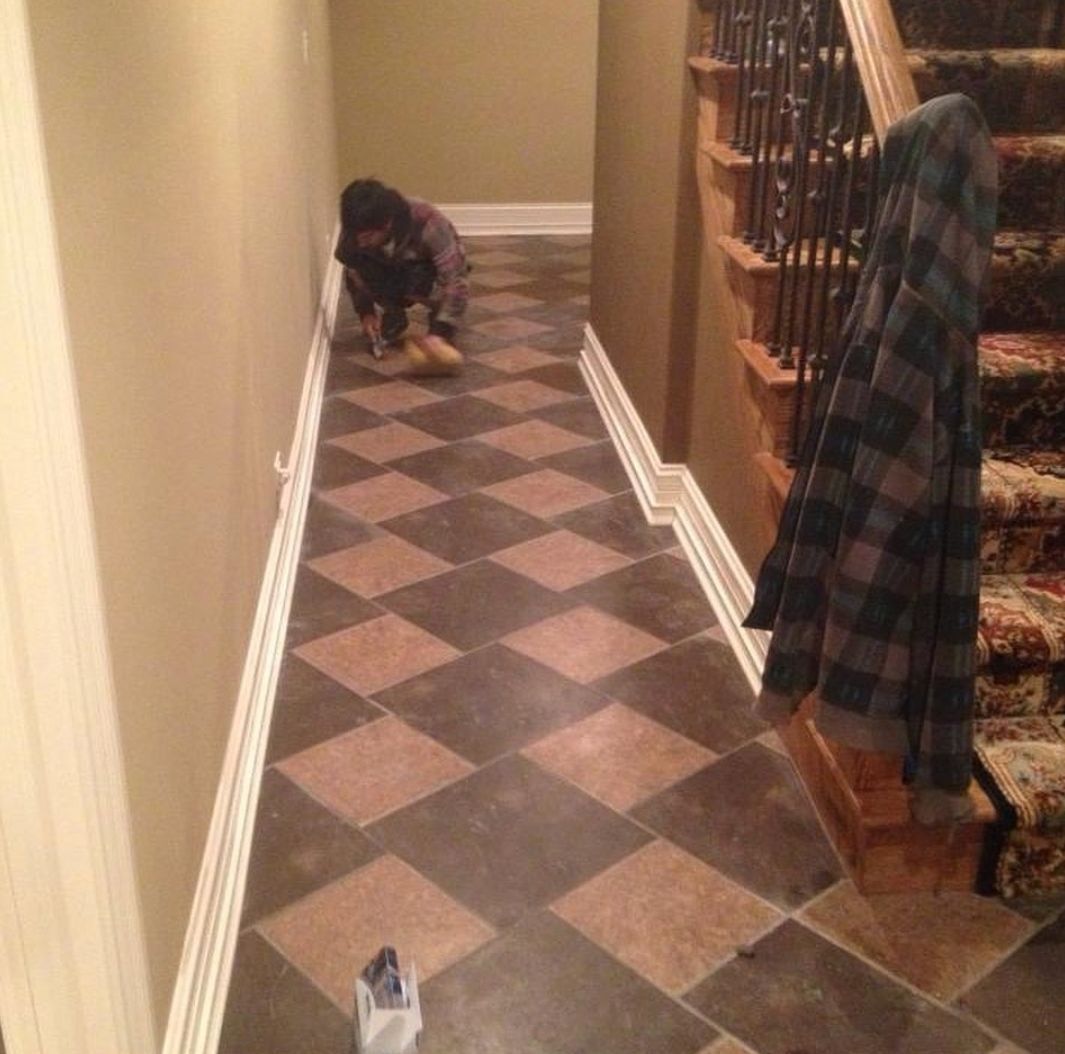 A person is working on a checkered floor in a hallway next to stairs