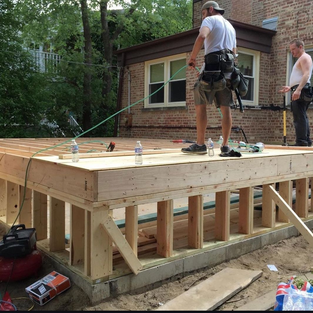 A man is standing on a wooden platform in front of a brick building.