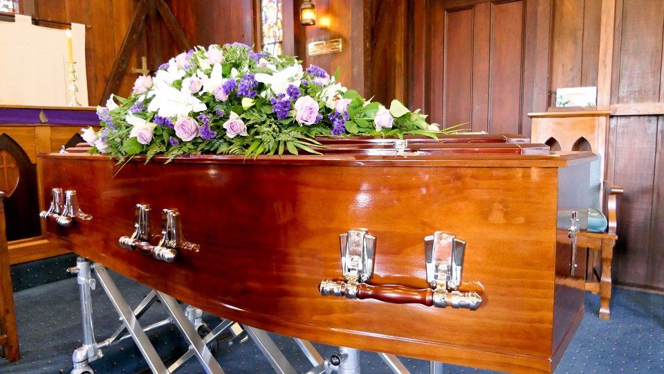 Bara durante funerale con cuscino di fiori bianchi e viola