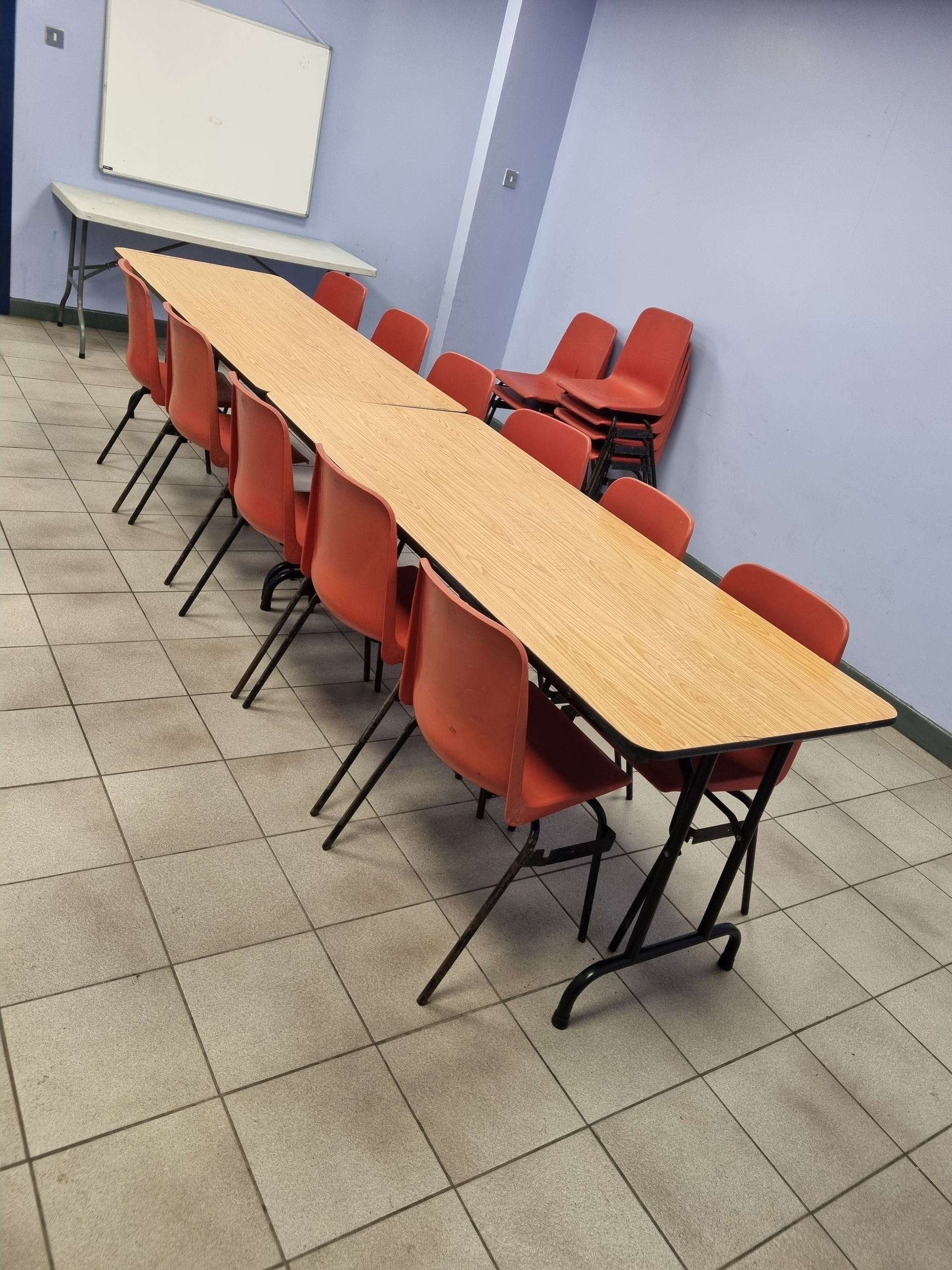 A long, rectangular table with several red chairs arranged in a room with light blue walls and a white whiteboard.