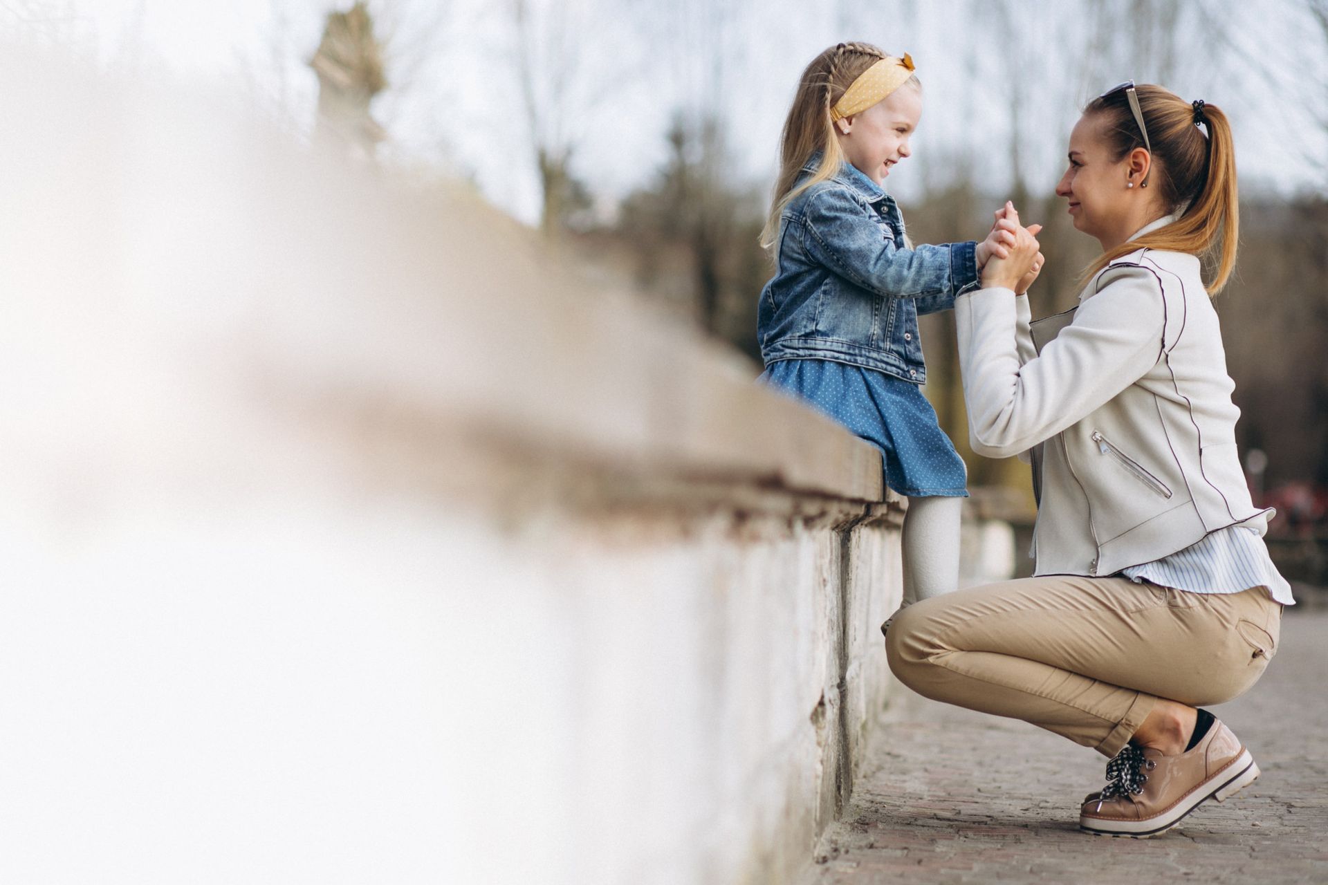 Woman kneels and holds hands with a child atop a concrete wall outdoors.