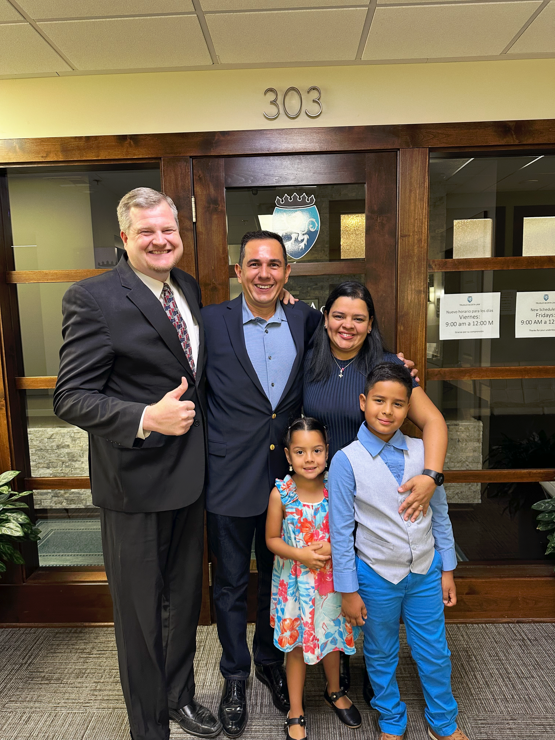 Two men and a family of three pose in front of a door.
