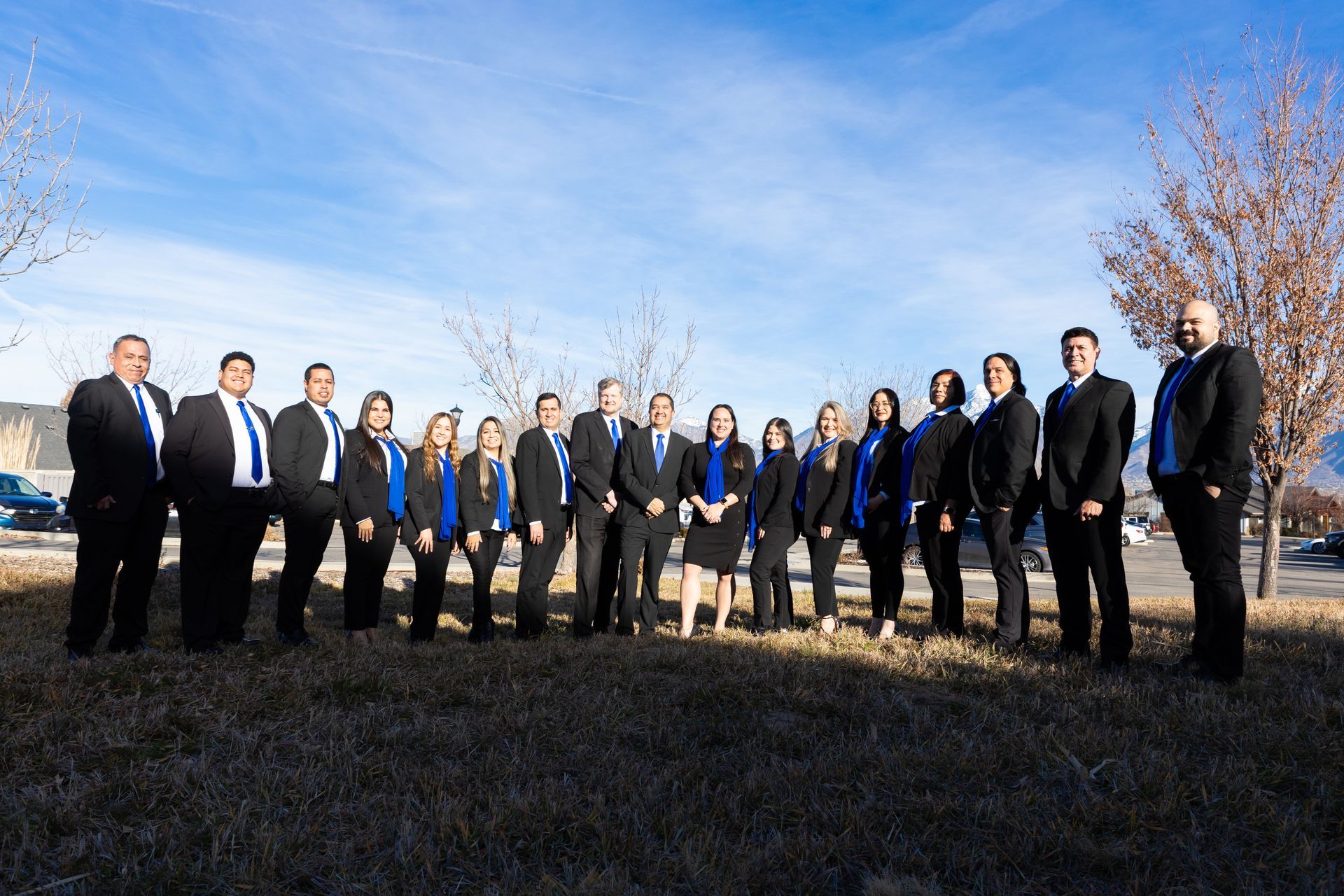 Group of people in suits and blue shirts standing outside on a sunny day.