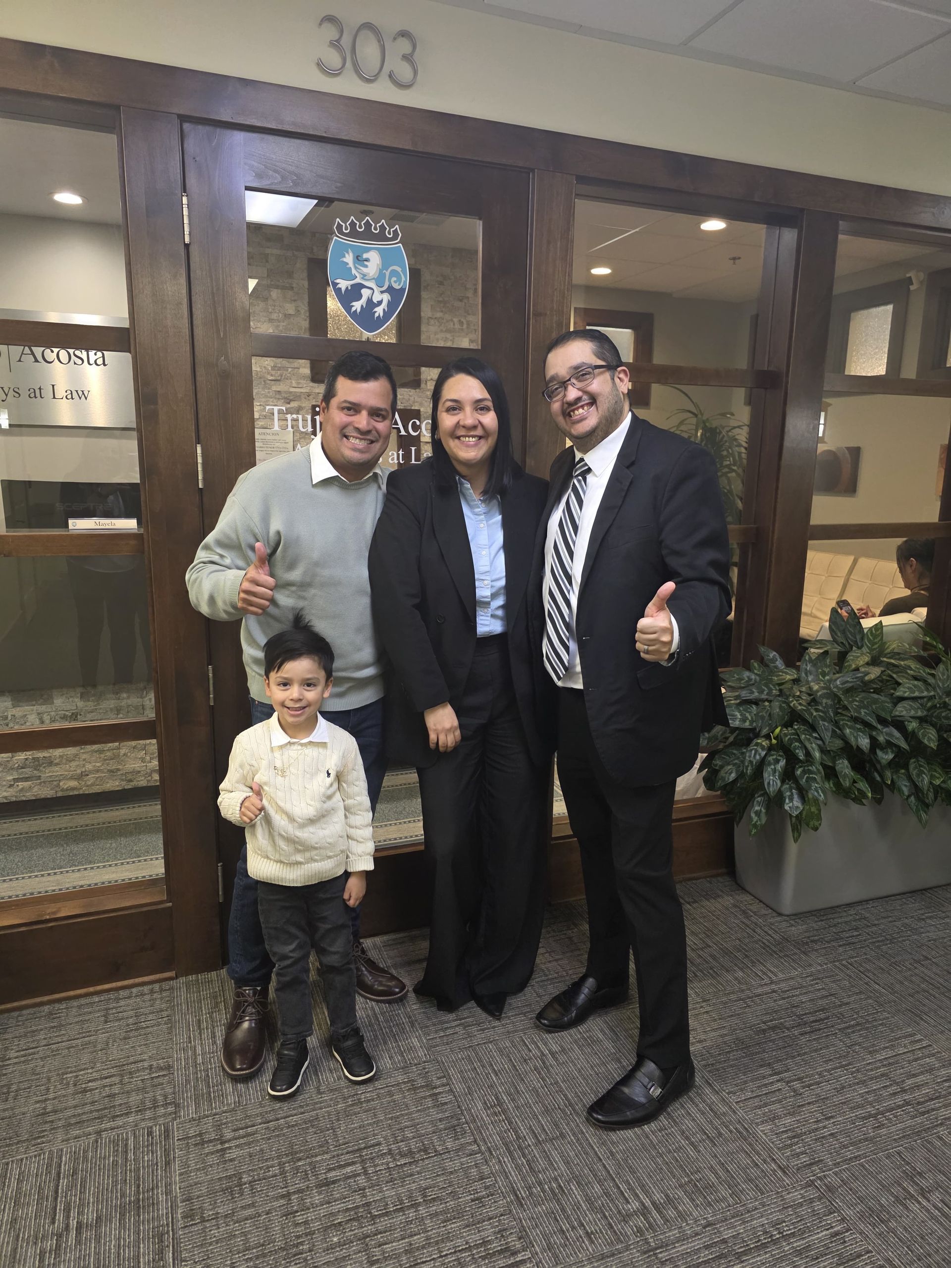 Four people smiling and giving thumbs up in front of an office door.