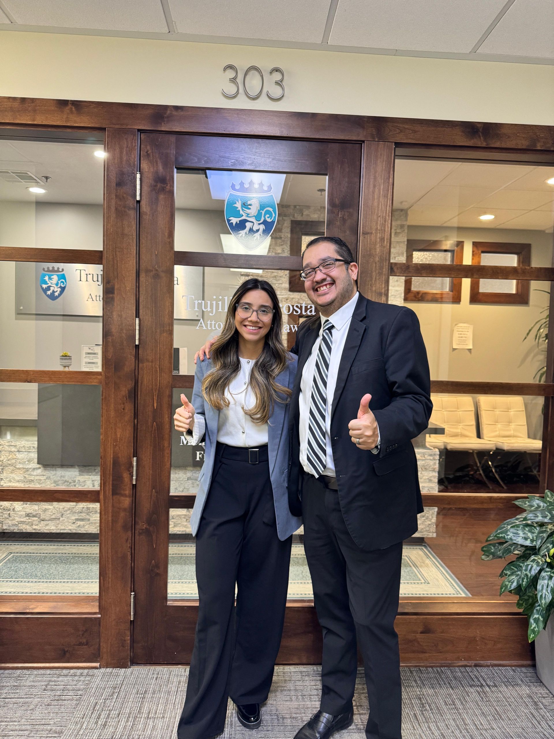 Two people giving thumbs up in front of an office door with the number 303 above it.